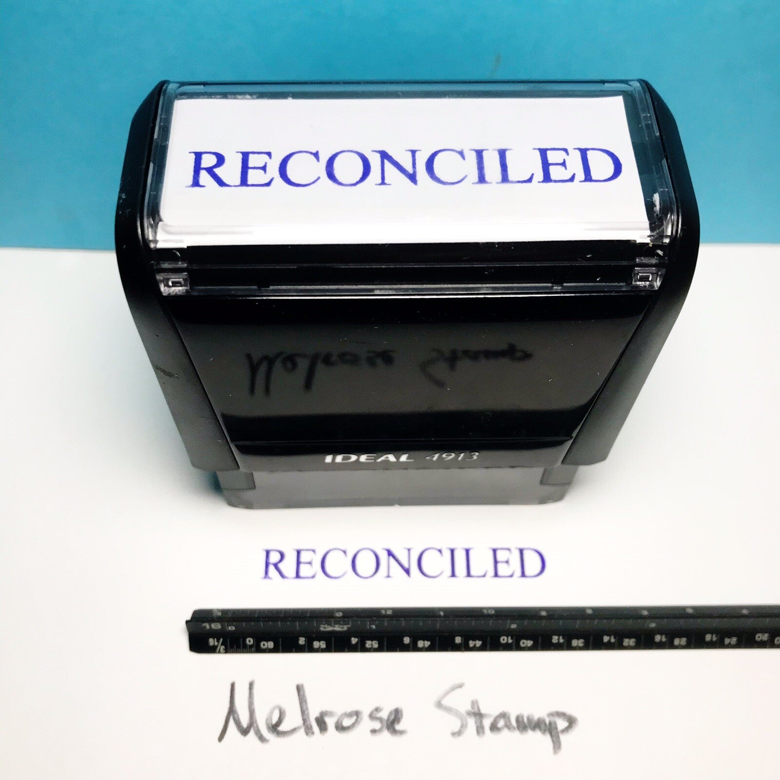 Rubber stamp with 'RECONCILED' text and a ruler for size reference on a blue and white background.