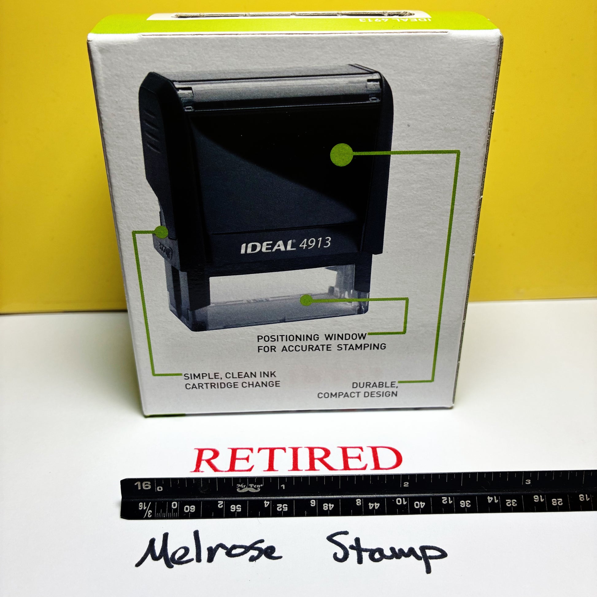 Black stamp with 'IDEAL 4913' branding on a white box against a yellow background, with a ruler at the bottom.