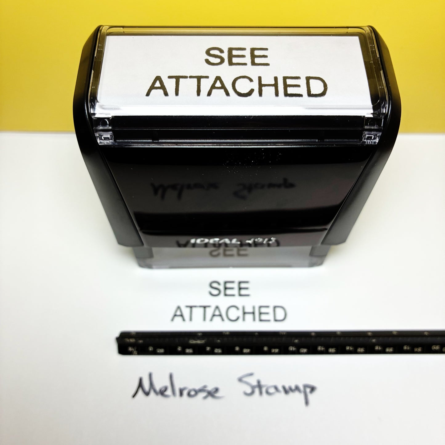 Rubber stamp with 'SEE ATTACHED' text on a white background