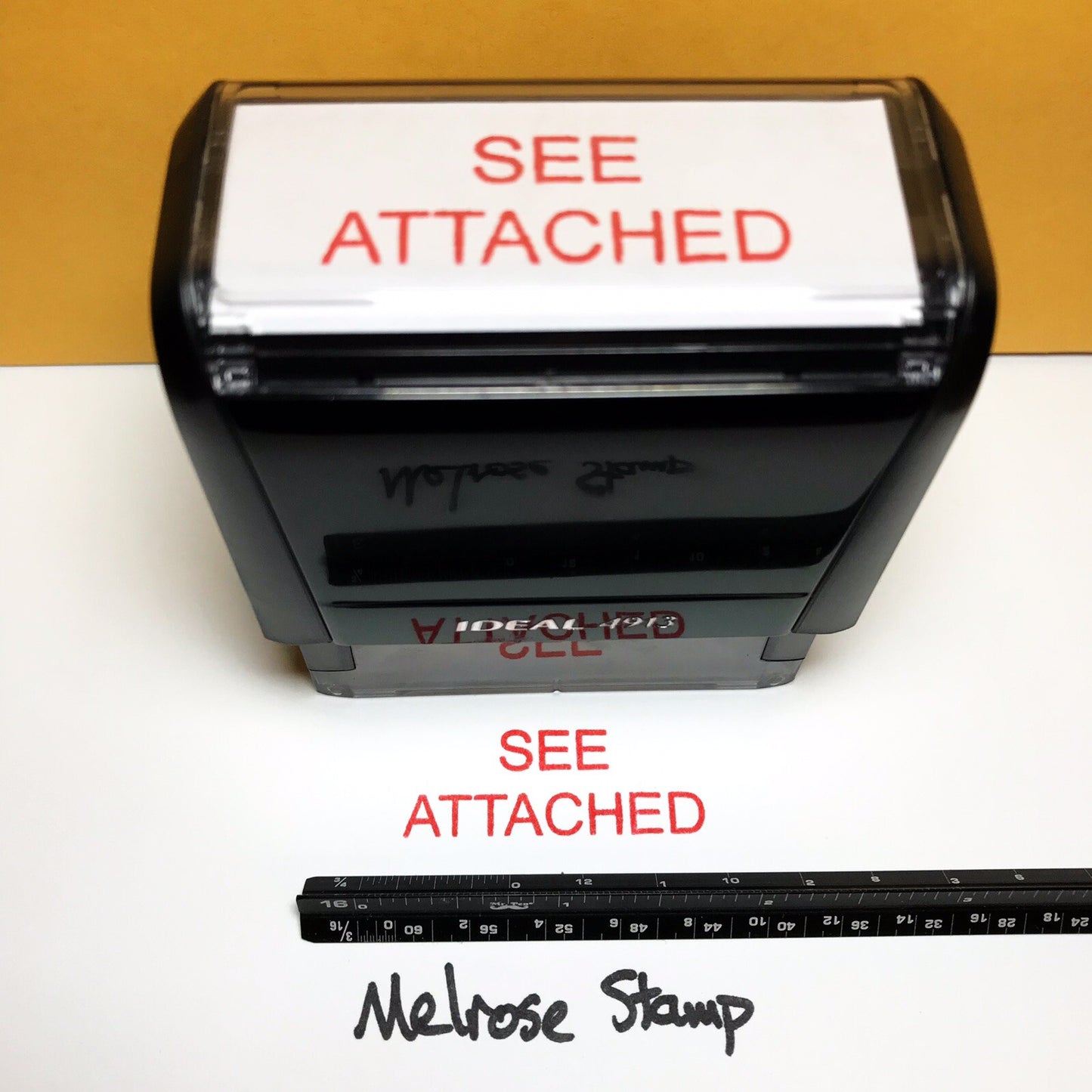 Rubber stamp with 'SEE ATTACHED' text on a white background