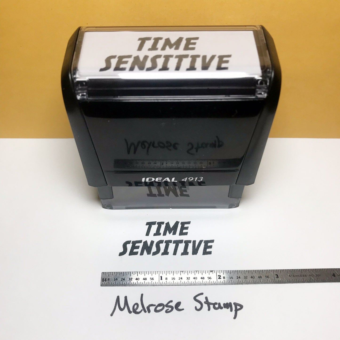 Rubber stamp with 'Time Sensitive' text on a white surface with a ruler for scale.