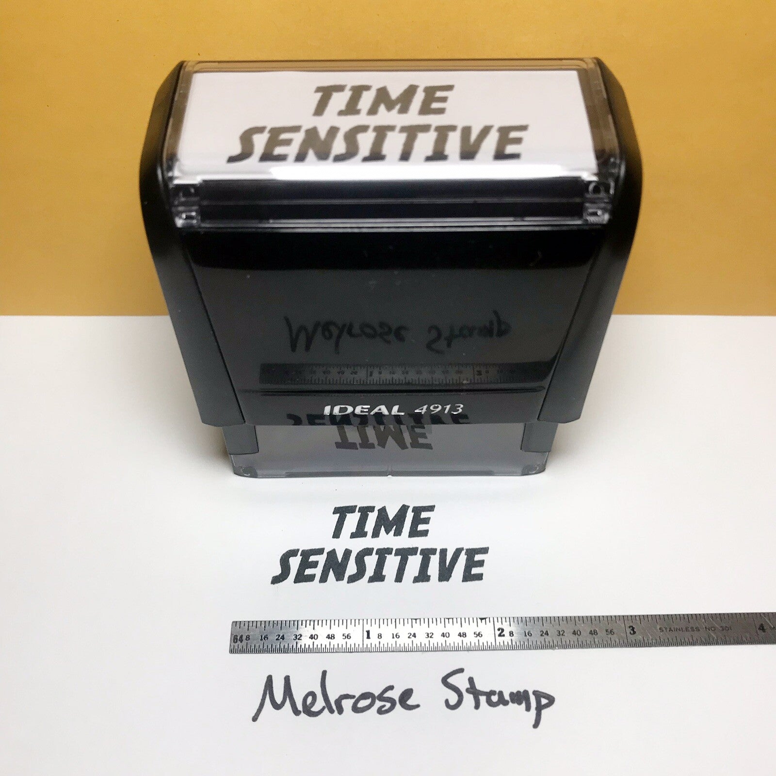 Rubber stamp with 'Time Sensitive' text on a white surface with a ruler for scale.