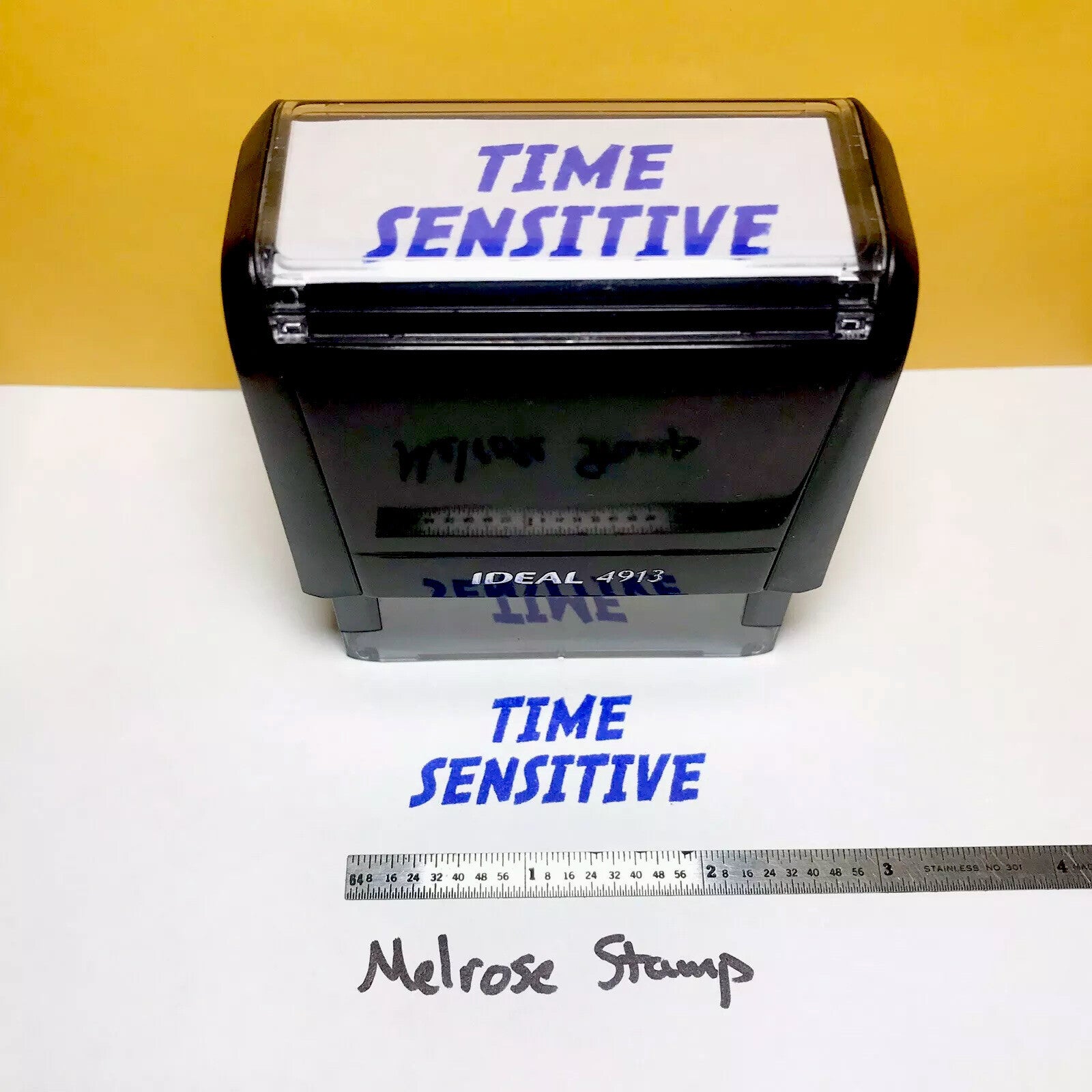 Rubber stamp with 'TIME SENSITIVE' text blue ink and a ruler for size reference on a white background.