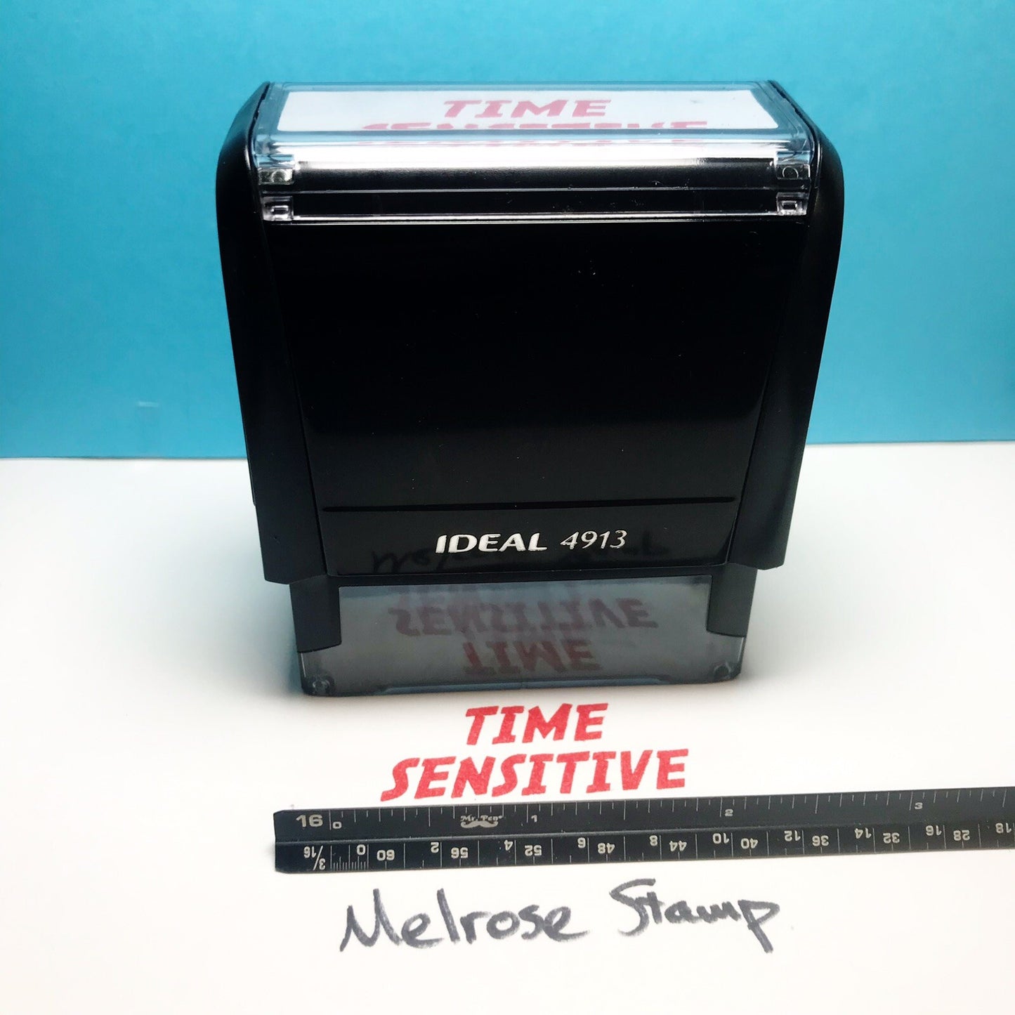 Rubber stamp with 'TIME SENSITIVE' text and a ruler for scale on a white surface.